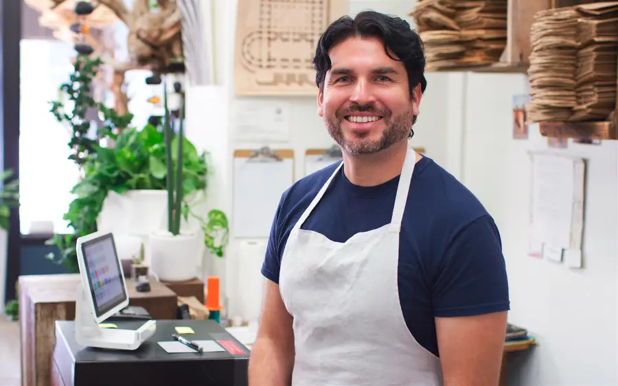 A shop owner in an apron at his counter